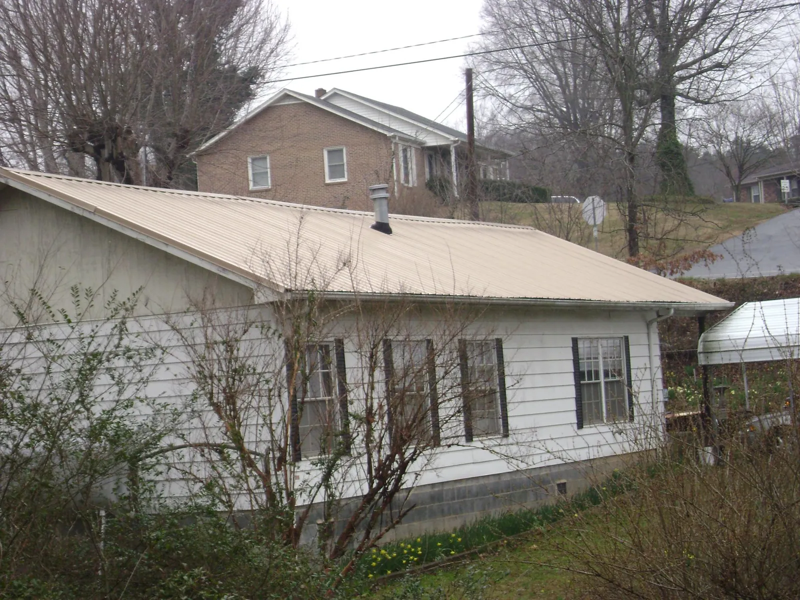 Tan metal roof on a white sided house set into a hillside — Commercial Roofing by Roofing Brothers in Chattaroy